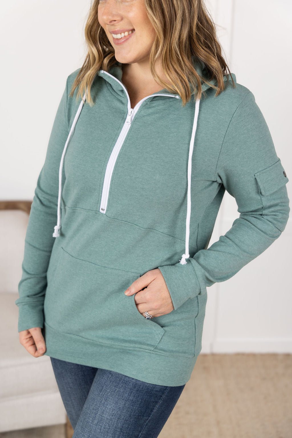 Sage color Pixie Pocket Halfzip Hoodie with triple stretch fabric, pocket on the sleeve, kangaroo pocket, and a feminine fit for comfort and style.